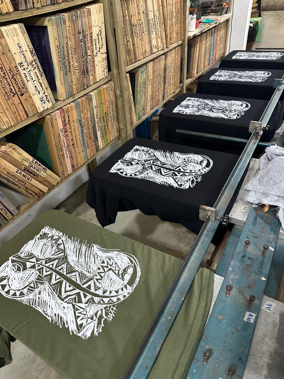 Camisetas pretas e verde-oliva com estampa artística na bancada de produção