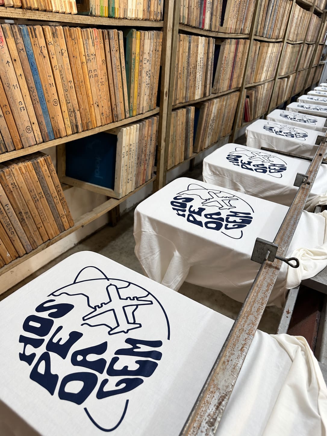 Camisetas estampadas alinhadas na bancada da Rebecchi, ao lado das matrizes de silk
